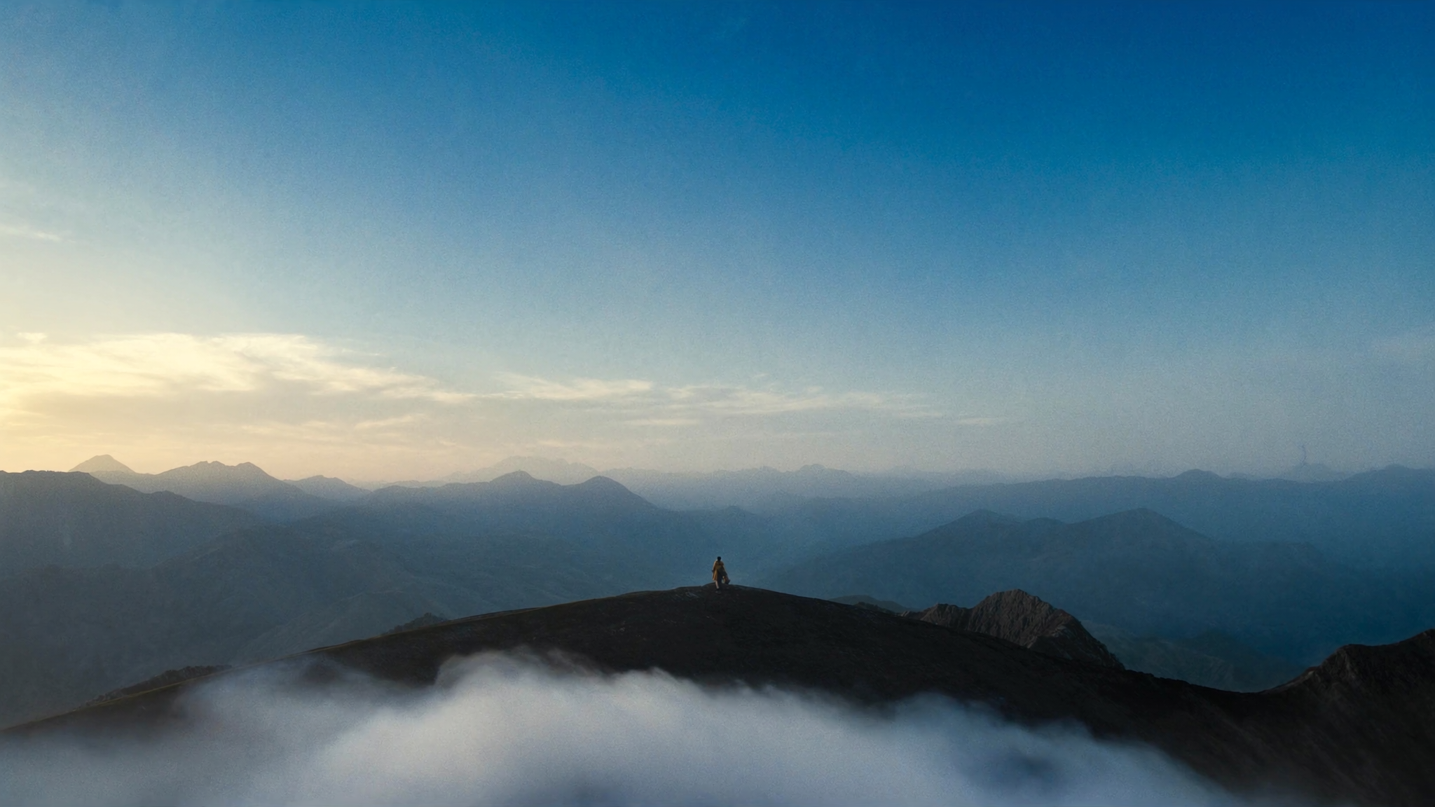 Mountain ridge at golden hour with low clouds drifting across the foreground.